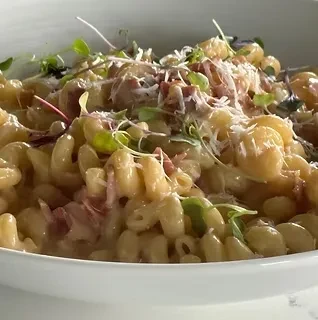 Creamy pasta with ham, cheese, and microgreens in a white bowl.