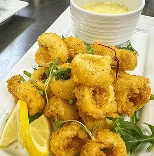 Golden-brown fried calamari, garnished with herbs and lemon wedges.