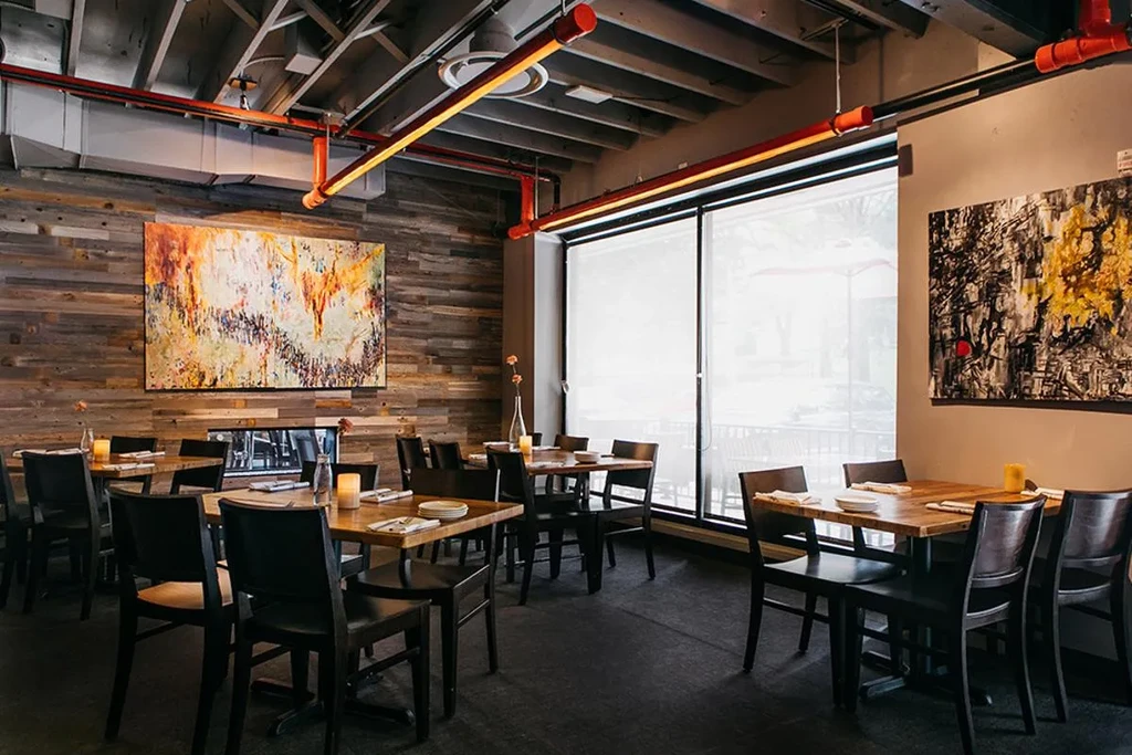 Industrial-chic restaurant with wooden tables, black chairs, and abstract paintings.