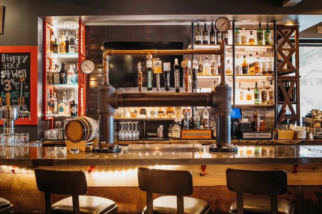 Industrial bar with multi-tap beer system and brightly lit liquor bottles.
