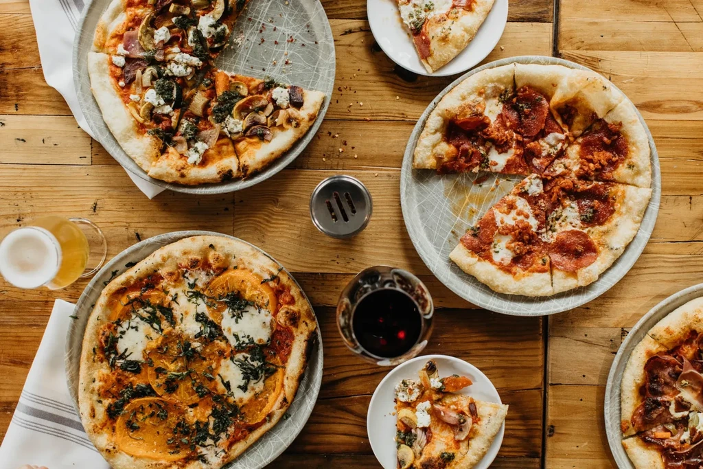Overhead view of a rustic table with diverse pizzas, beer, and wine.