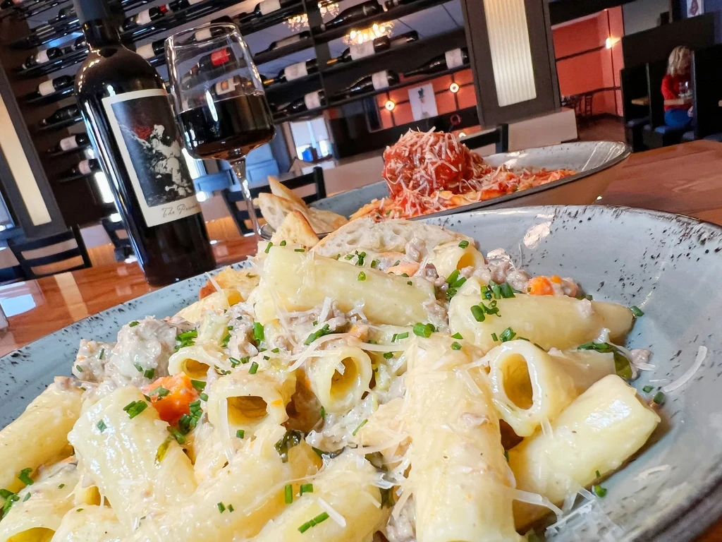 Rigatoni, meatball pasta, and red wine on a restaurant table.