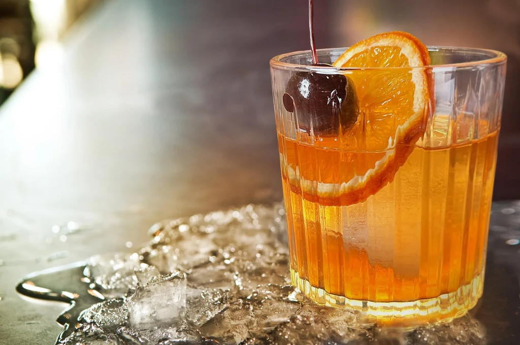 Amber cocktail in ridged glass with orange slice and cherry.