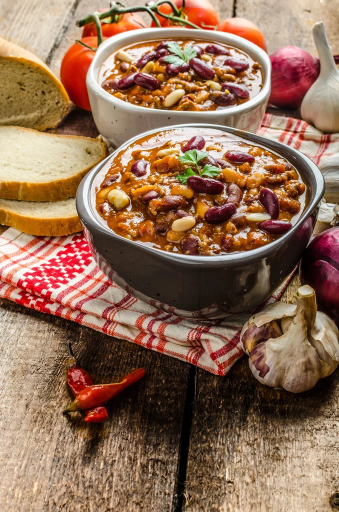 Two bowls of chili and fresh ingredients on a rustic wooden table.