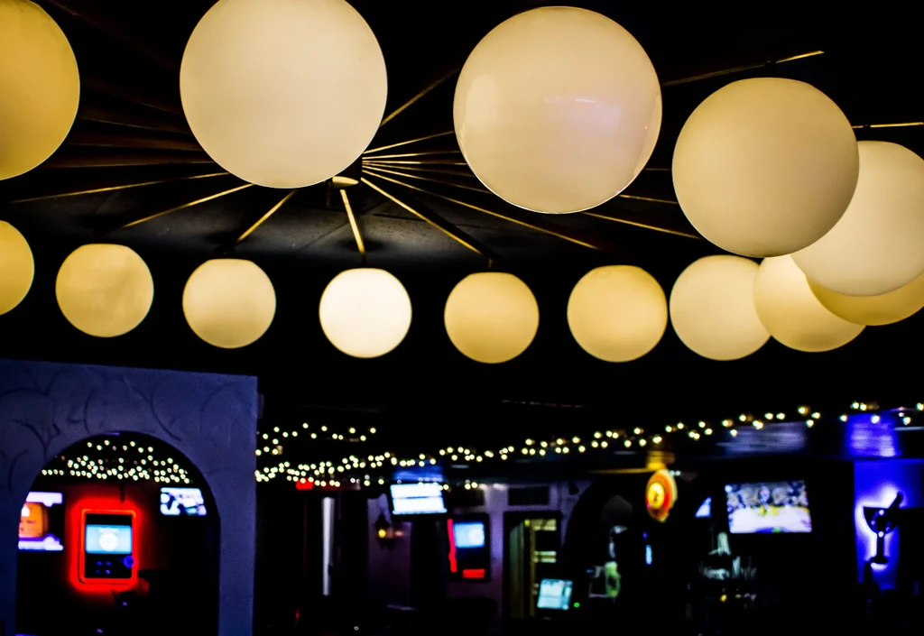 Dimly lit bar interior featuring many cream globe lights and screens.