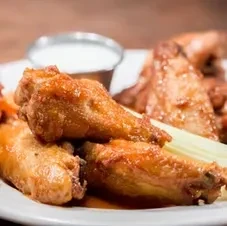 Golden-brown glazed chicken wings with white dipping sauce and celery.