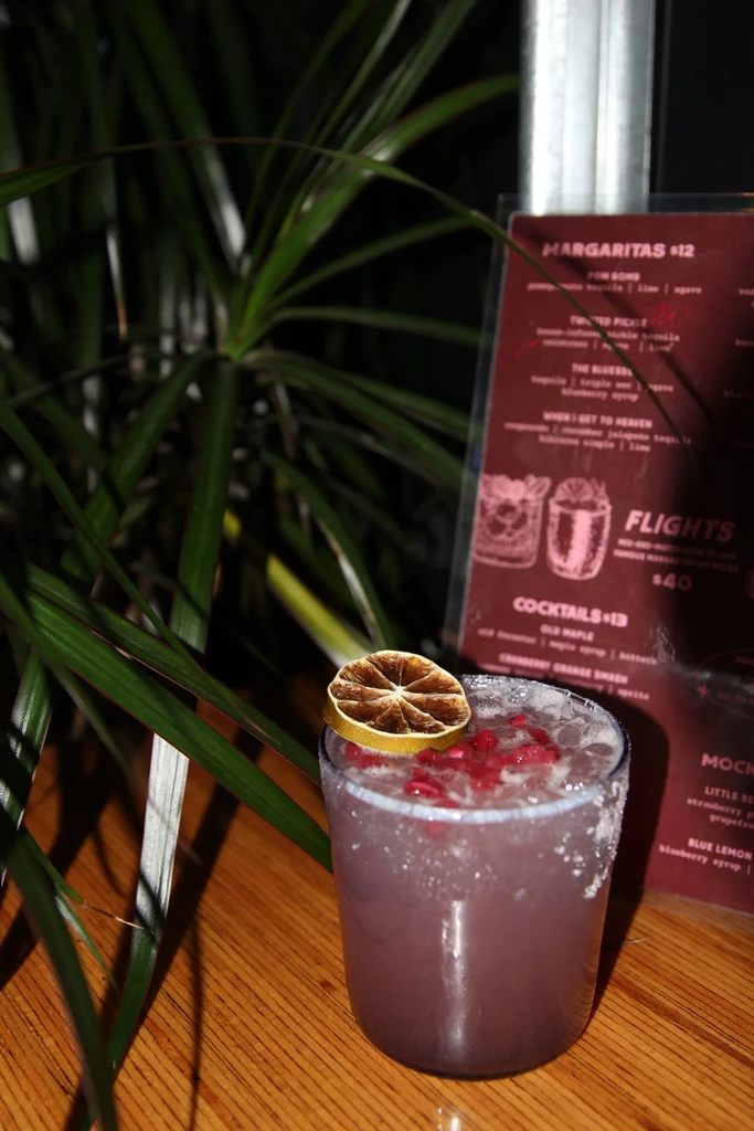 Lavender cocktail in textured glass, garnished with berries, citrus, and menu.