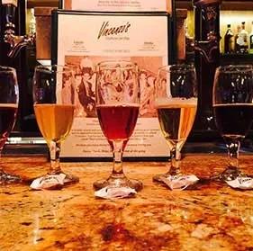 Four stemmed drinks on a bar, Vincent's menu clearly visible.