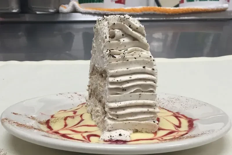 Frosted multi-layer cake with dark specks, plated with decorative sauce.