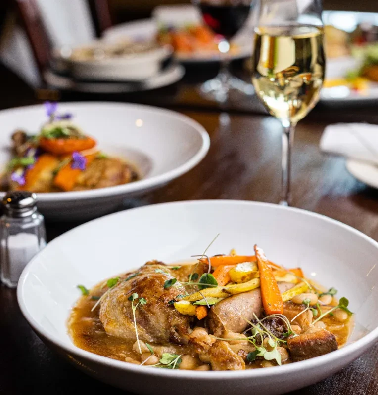 Plated stew with golden meat, sausage, beans, carrots, and microgreens.