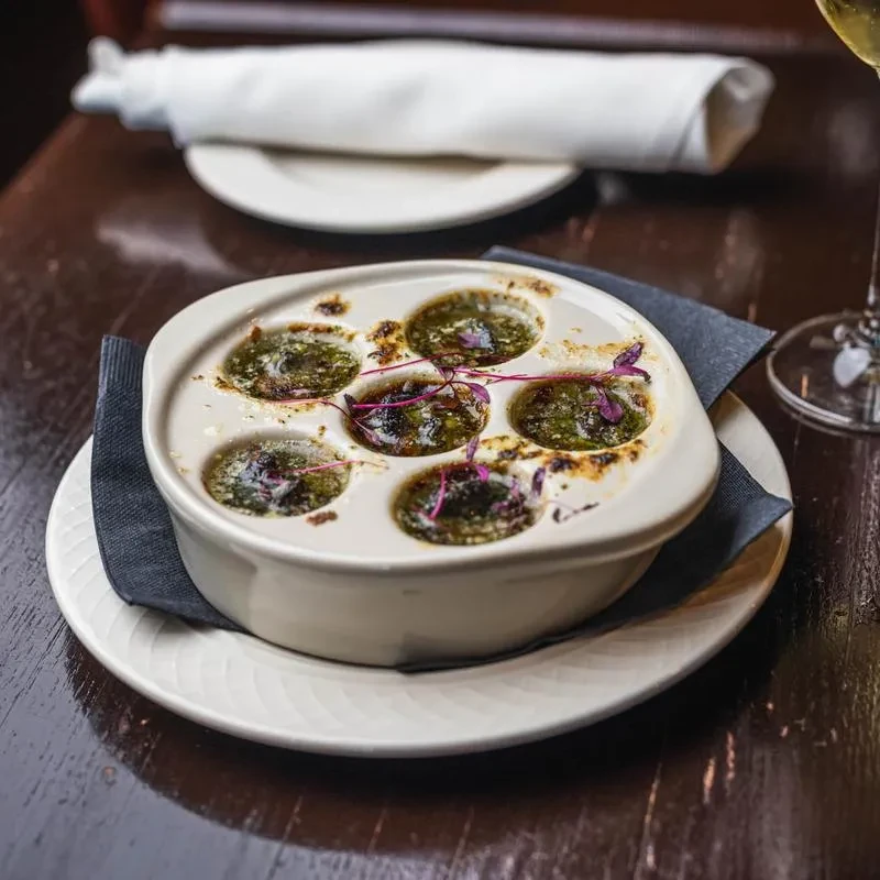 Six escargots in green herb-butter sauce, garnished with purple sprouts.