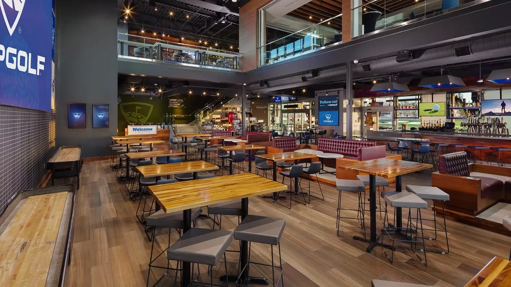 Topgolf venue interior with multi-level dining, bar, and shuffleboard.