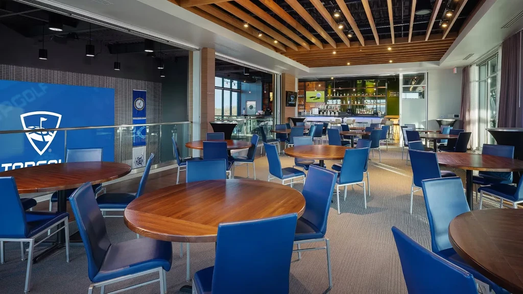 Empty Topgolf dining area with blue chairs and bar.