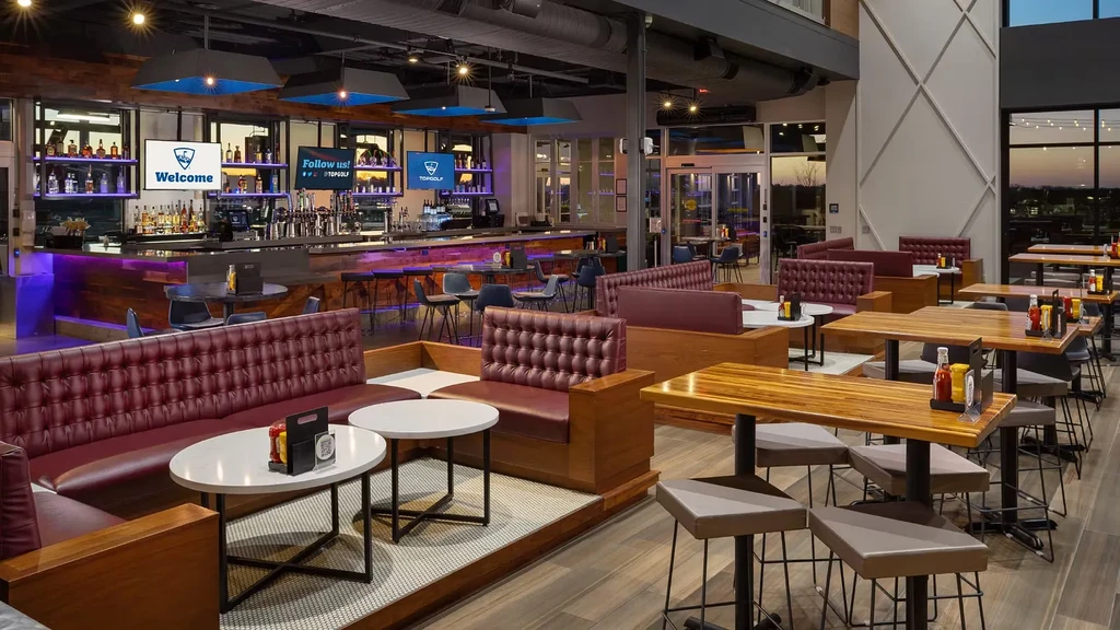 Modern, empty Topgolf restaurant interior with a bar and diverse seating.