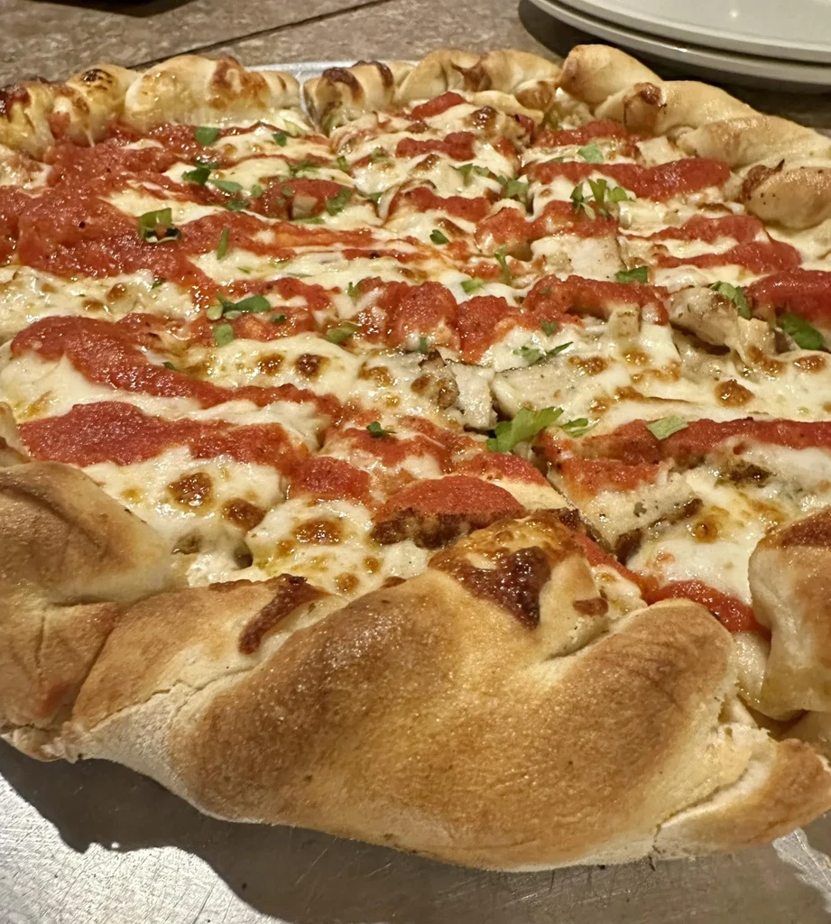 Top-down of a sliced stuffed crust pizza with cheese, chicken, and herbs.