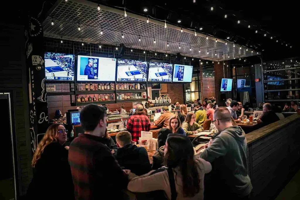 Lively sports bar interior with patrons, multiple TVs, and a stocked bar.