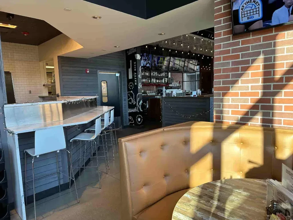 Bright modern restaurant interior: booth, counter, and bar with screens.