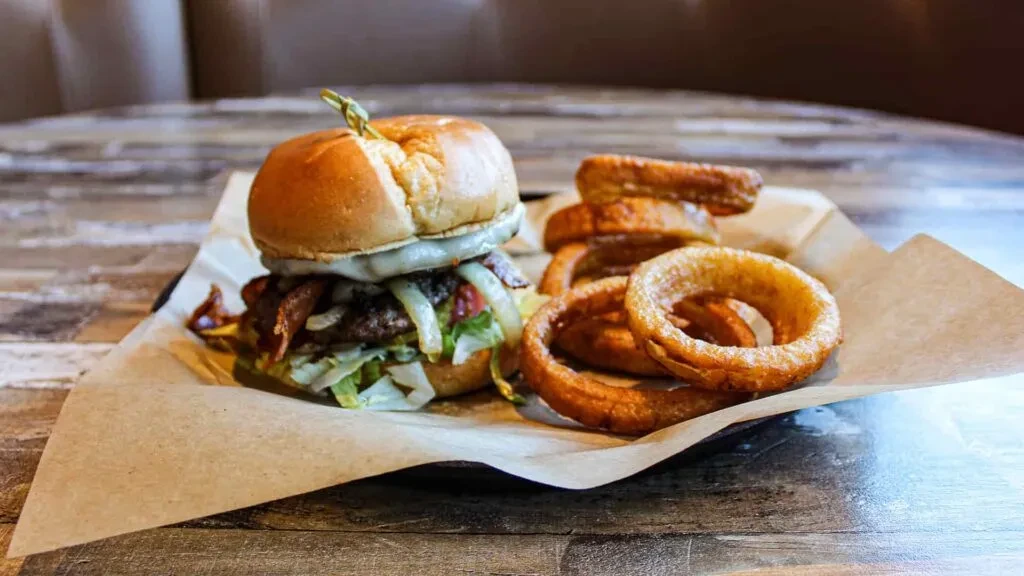 Close-up of a substantial burger with bacon, cheese, and crispy onion rings.