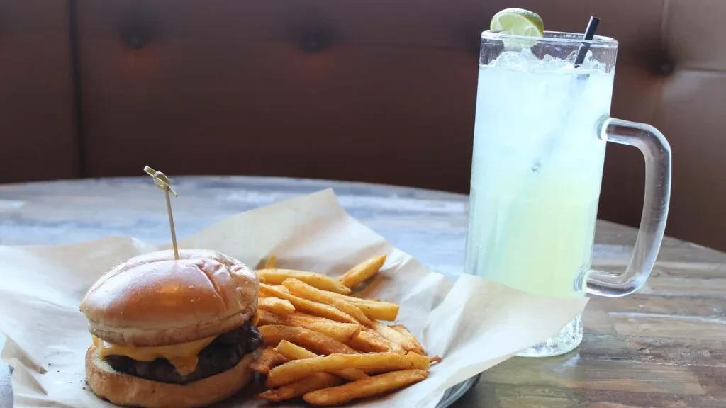 Cheeseburger, french fries, and light green drink on a wooden table.