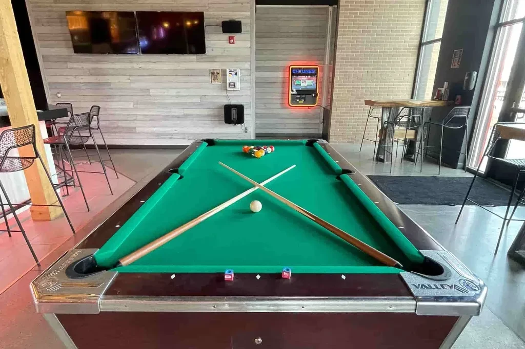 Modern bar with a green pool table and a neon jukebox.
