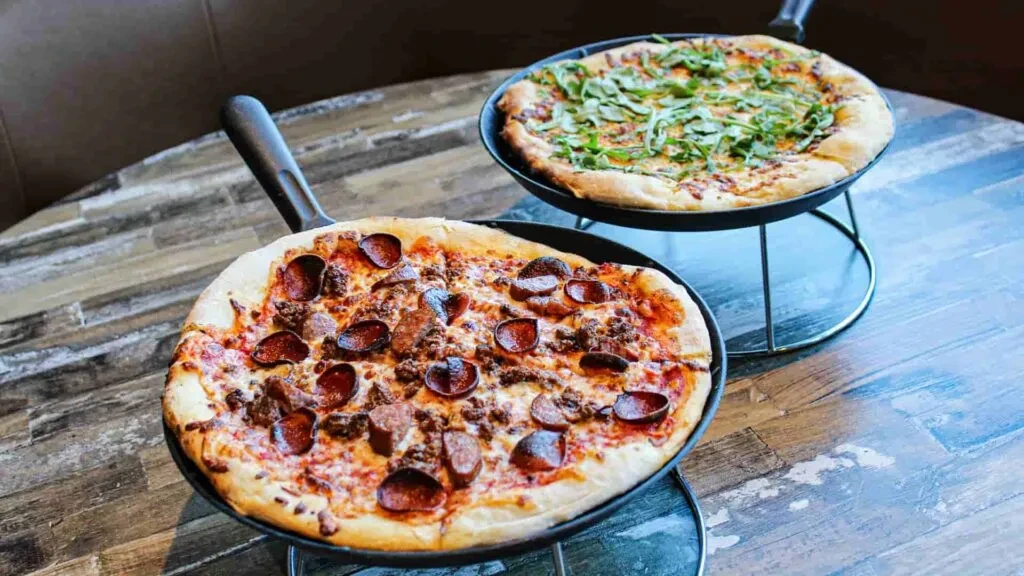 Two pizzas: pepperoni and leafy green, served on elevated pans.