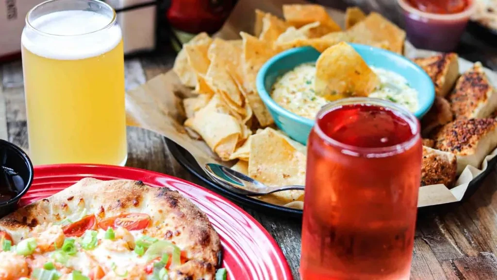 Pizza, tortilla chips, garlic bread, and drinks on rustic table.