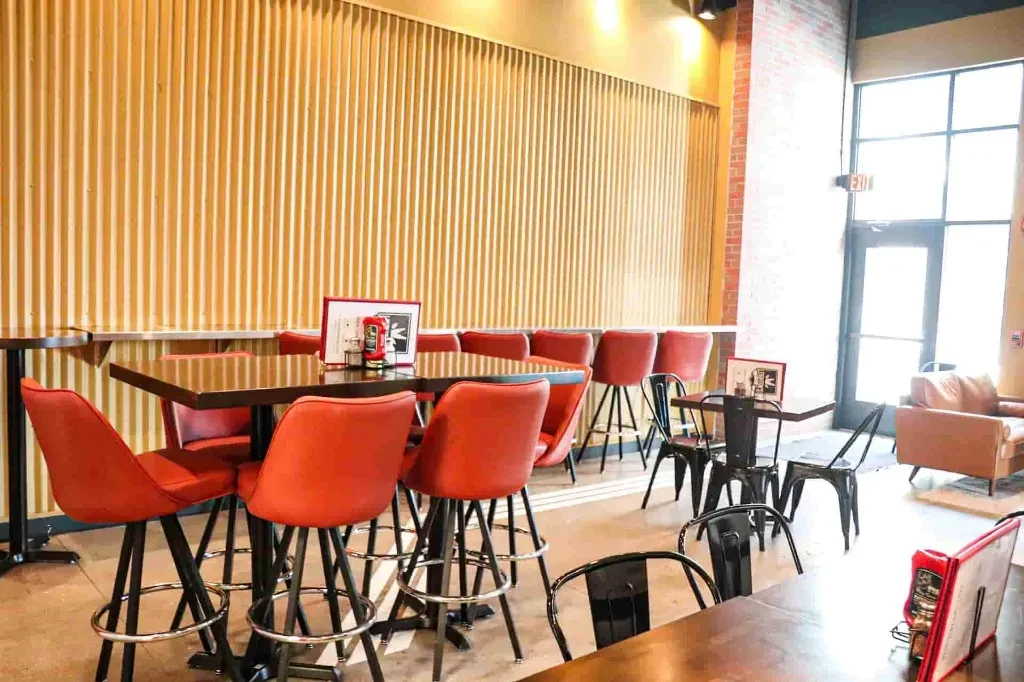 Modern restaurant with high-top tables, red bar stools, and a wooden wall.