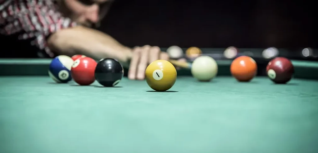 Yellow '1' billiard ball on green felt, player preparing shot.