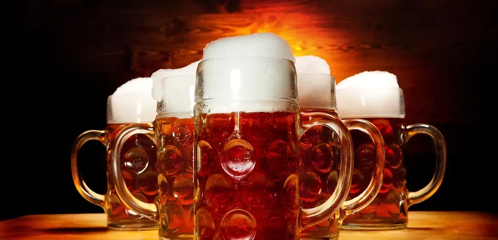Five large steins of amber beer with frothy heads.