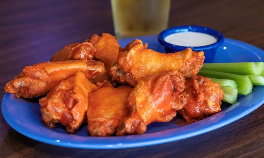 Blue plate of buffalo chicken wings, celery, and dip.