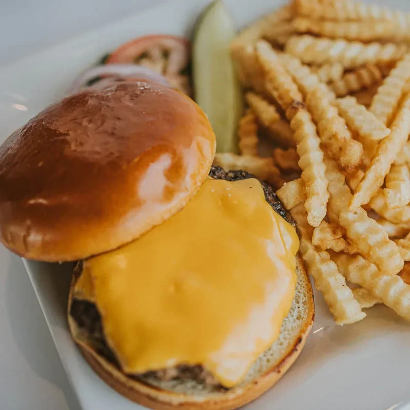 Classic cheeseburger, fries, and pickle on a white plate.