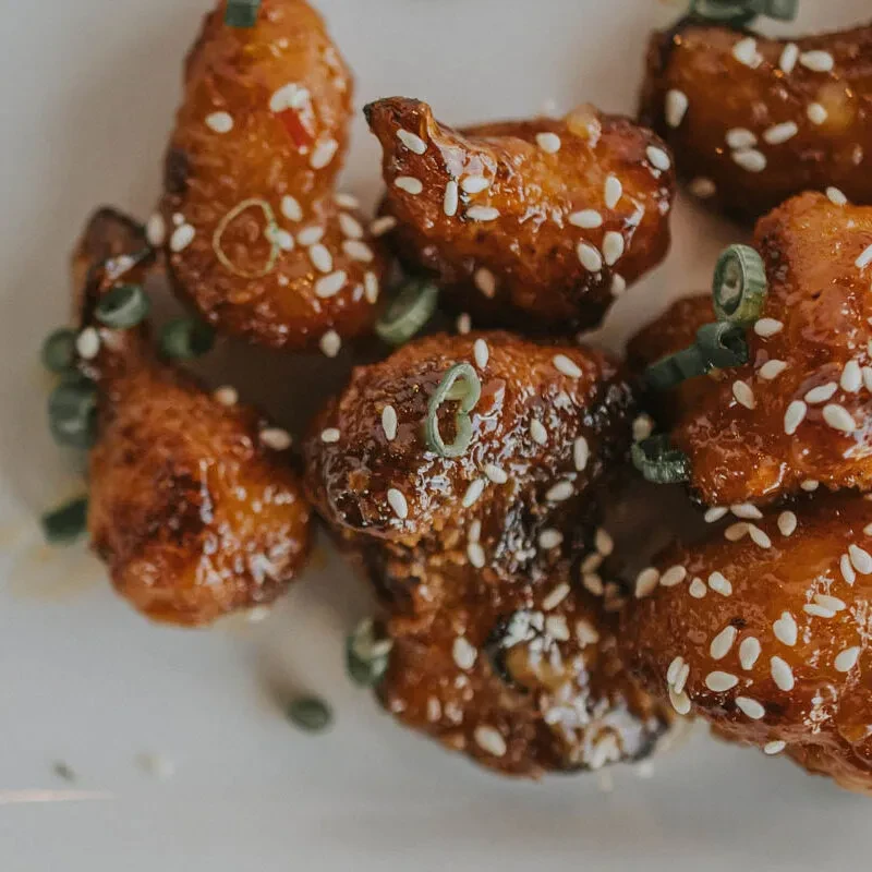 Reddish-brown glazed chicken with sesame, green onions, and chili flakes.
