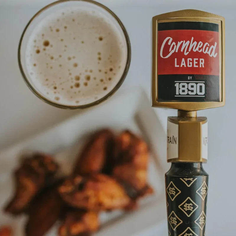 Top-down: beer glass, "Cornhead LAGER" tap handle, and chicken wings.