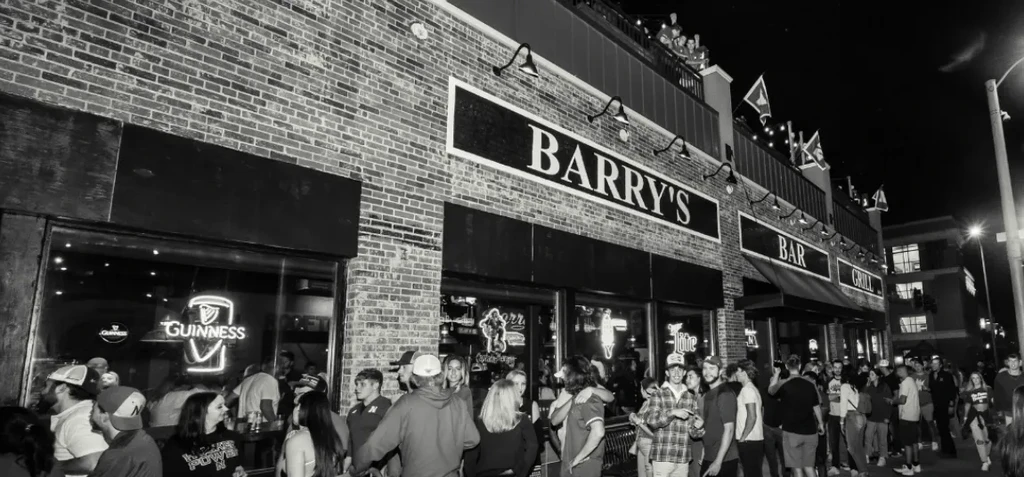 Black and white photo: Barry's Bar Grill, busy with people at night.