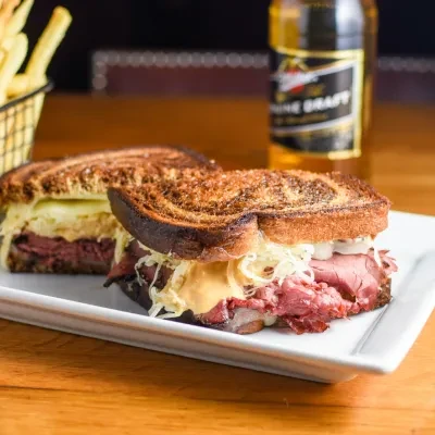 Reuben sandwich, cut in half, on a plate with fries and beer.