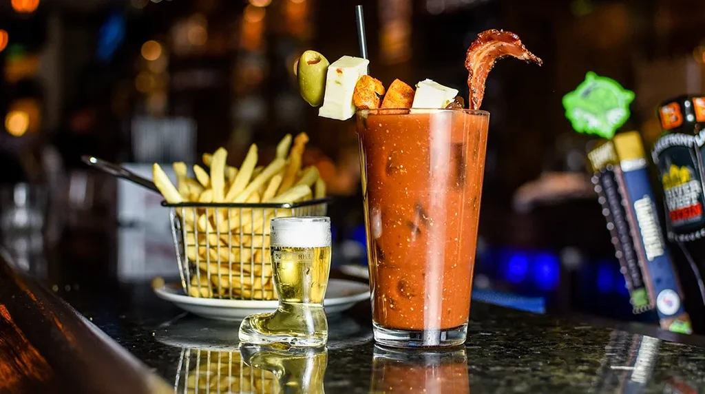 A garnished Bloody Mary, miniature beer, and fries at a bar.