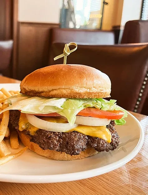 Well-stacked burger with cheese and fries on a plate in a restaurant.