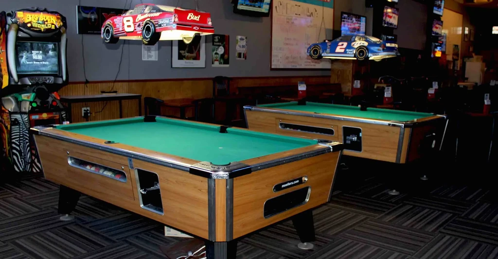 Two pool tables and an arcade game in a dim sports bar.