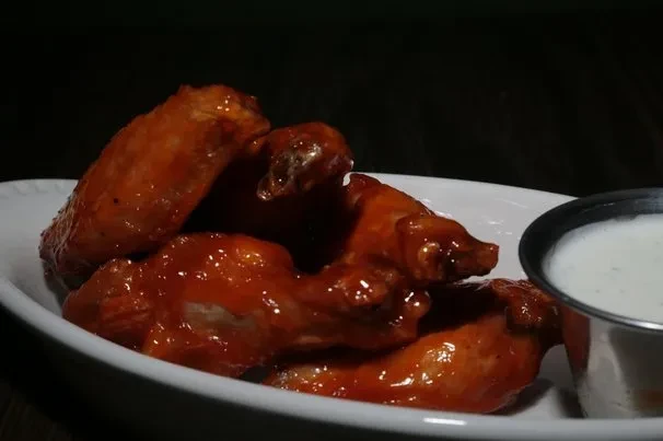 Close-up of glossy, reddish-orange chicken wings with white dipping sauce.