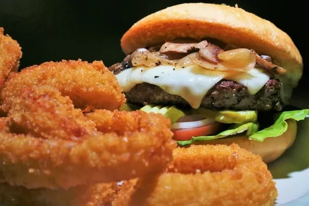 Gourmet beef burger with melted cheese, mushrooms, and onion rings.