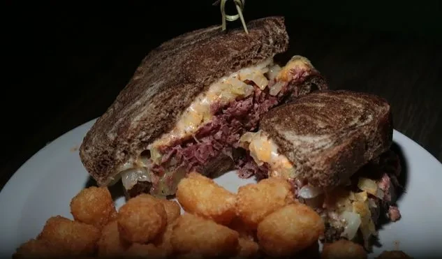 Halved Reuben sandwich with corned beef, sauerkraut, cheese, and tater tots.