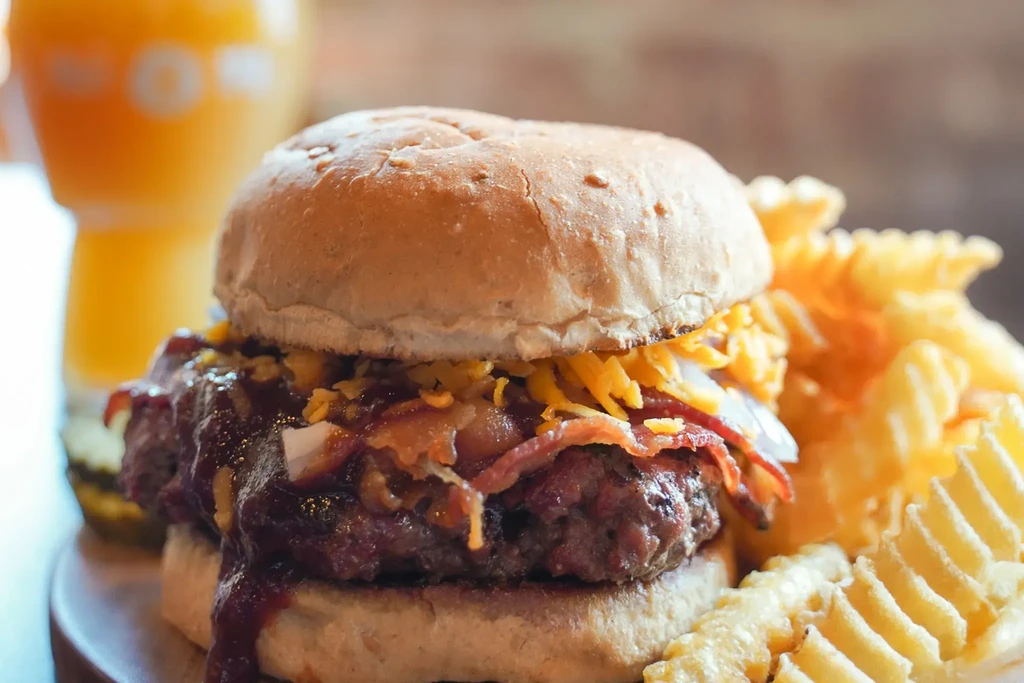 Burger with melted cheese, bacon, barbecue sauce, and waffle fries.