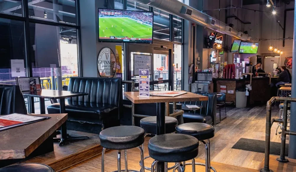 Modern sports bar interior with seating, flat-screen TVs, and a stocked bar.