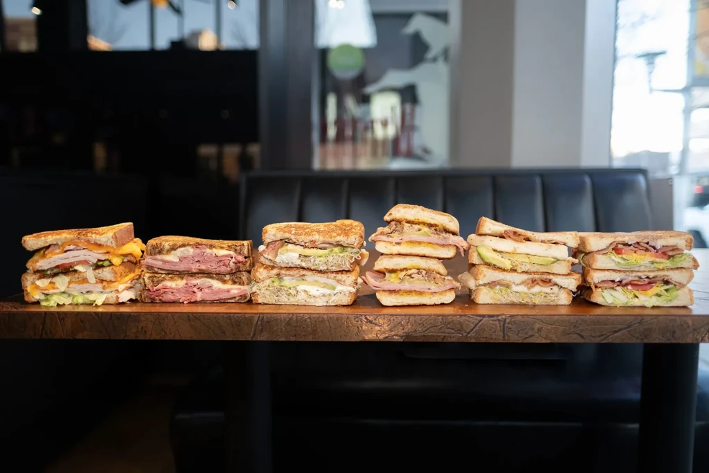 A row of six gourmet sandwiches with various fillings on a wooden table.