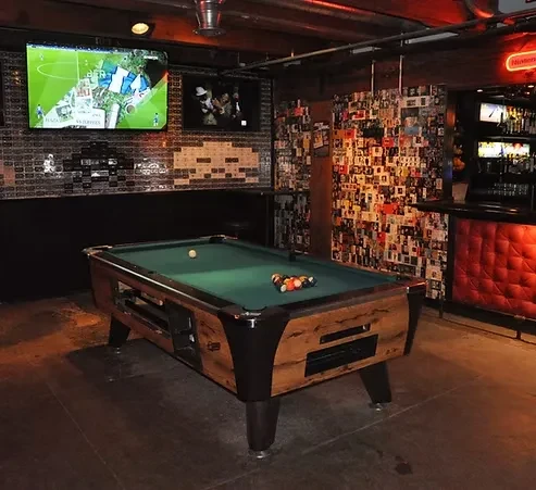 Interior of a dim bar with a pool table, red bar, and TVs.