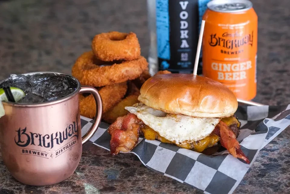 Burger with egg, bacon, onion rings, and Brickway branded drinks.