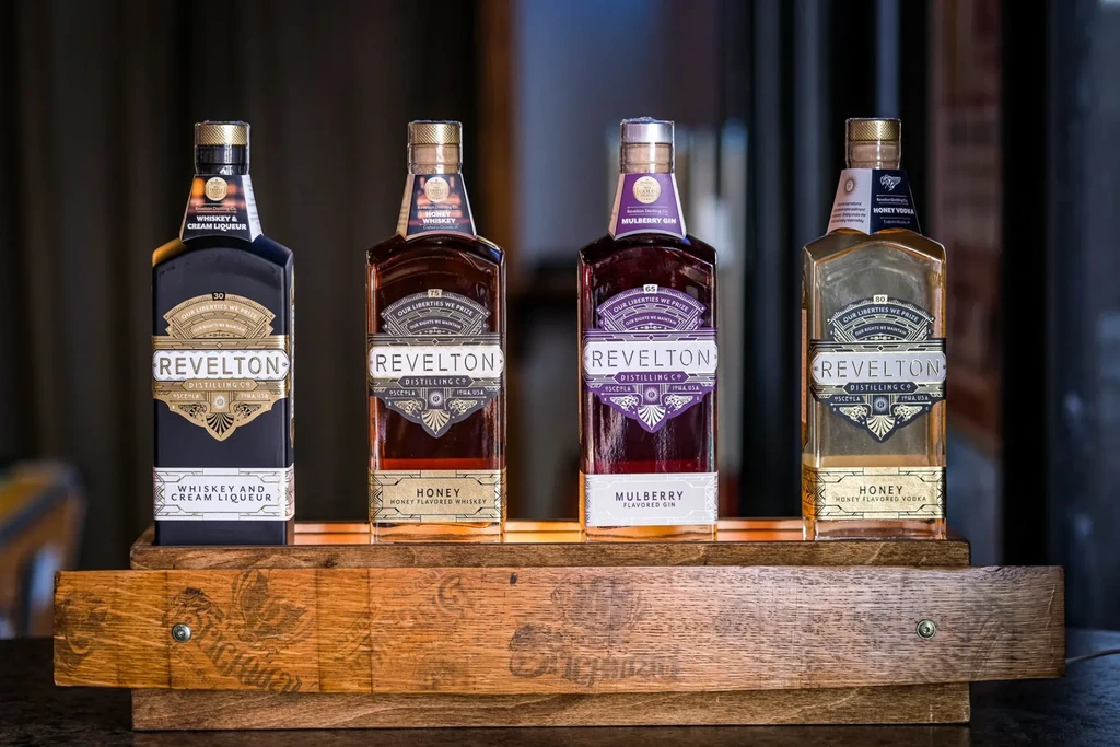 Four Revelton spirits: Whiskey, Gin, Vodka, Liqueur, on a wooden stand.