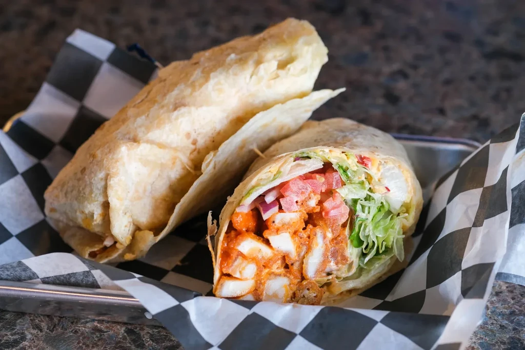 Cut burrito with chicken, lettuce, tomato, onions in a metal tray.