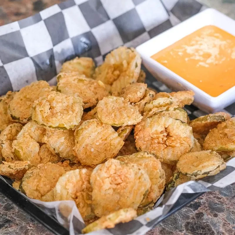 Crispy golden-brown fried pickles in a basket with dipping sauce.