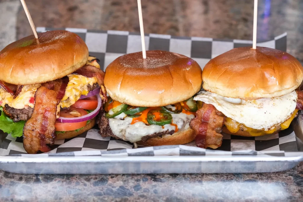 Three gourmet burgers: pimento, jalapeño, and fried egg on a tray.